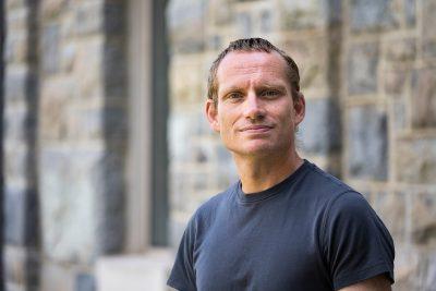 Robert Weiss poses in a t-shirt in front of a  Hokie Stone building. 