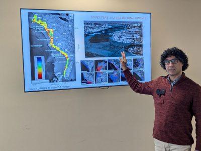 Manoochehr Shirzaei gestures at a screen with the a graphic and the title: "Sinking land on the U.S. East Coast."