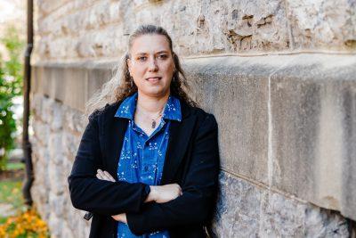 Woman stands with arms crossed next to building covered in Hokie Stone